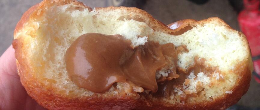 Brown cream oozes out of a half eaten bread roll.