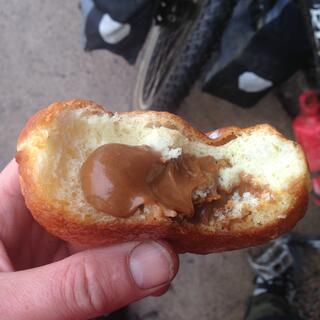 Brown cream oozes out of a half eaten bread roll.