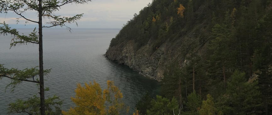 A forested hill ends in rocky walls rising from the lake.