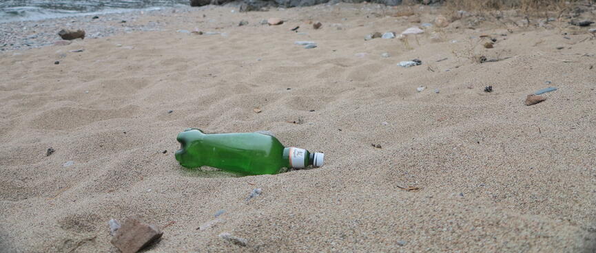A clear green beer bottle on a sandy beach.