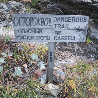 A bilingual wooden sign shows a hiker falling down a rocky bank.