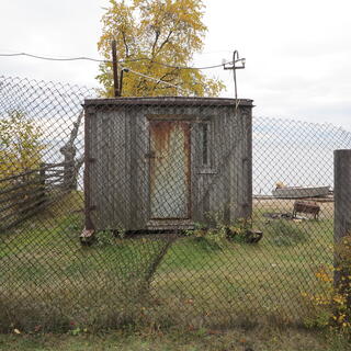 A rusty hut behind a wire mesh fence.