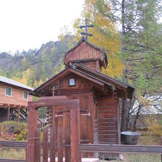 A very small wooden church sits behind a tall wooden gate.
