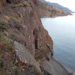 The trail clings to the cliffside, above the opening to a cave just above the waterline.