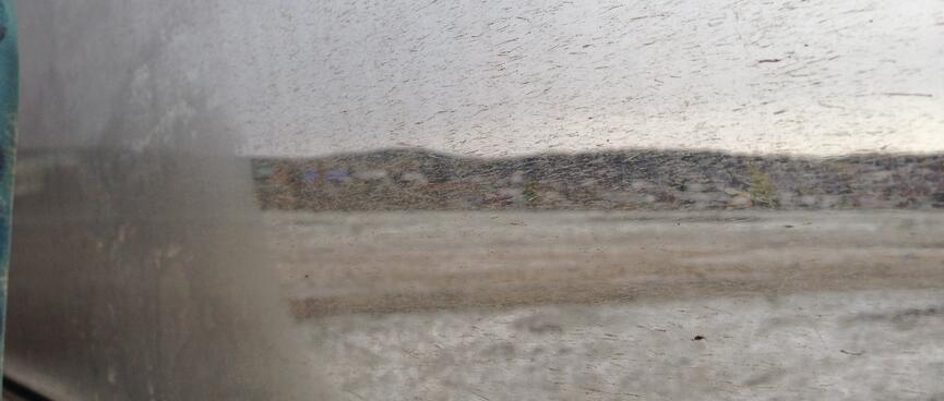 Hills and snow covered ground seen through a dirt spattered window.