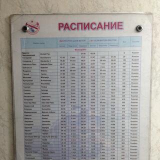 An rectangular sign titled 'РАСЛИСАНИЕ' (schedule) containing columns of places and times.